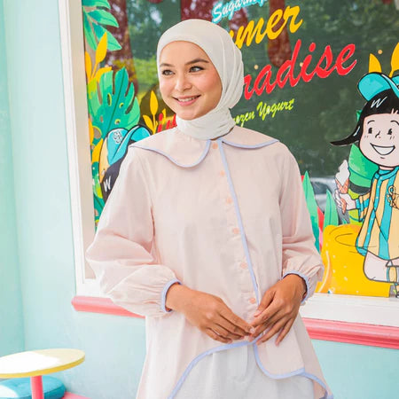 Woman in a light pink shirt with light blue list by Casa Elana standing in front of a colorful mural with cartoon characters.