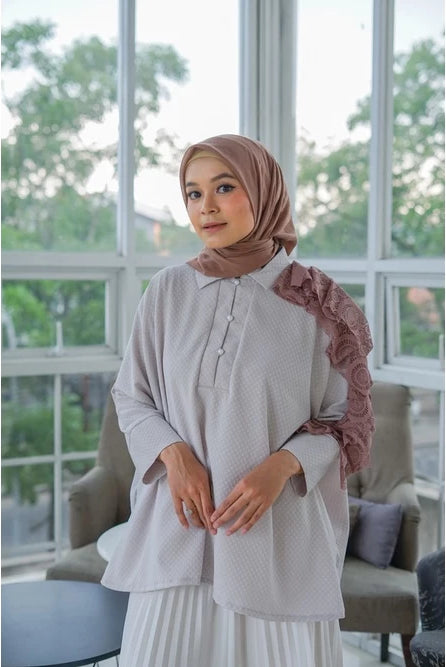 Woman wearing a light-colored shirt by Abame with ruffled sleeves in a room with large windows.