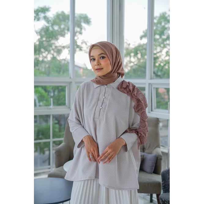 Woman wearing a light-colored shirt by Abame with ruffled sleeves in a room with large windows.