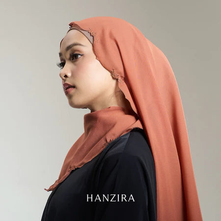 A woman wearing an orange pashmina scarf with embroidery, branded by HANZIRA.