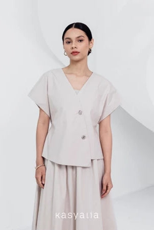 A woman wearing a beige, asymmetrical button-down blouse with short sleeves and a round neckline by Kasyalia.