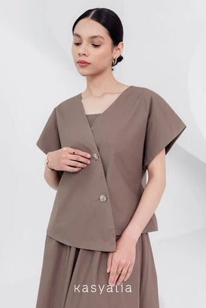 A woman wearing a brown, asymmetrical button-down blouse with short sleeves and a round neckline by Kasyalia.