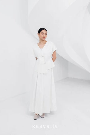 A woman wearing a white, asymmetrical button-down blouse with short sleeves and a round neckline by Kasyalia.