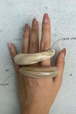 Hand wearing two beige acrylic bangle by Darje on a light gray background
