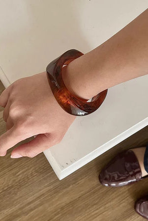 Person wearing a brown acrylic bracelet by Darje on a white surface with a wooden floor.
