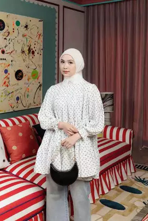 Woman standing in a room wearing white polka dot blouse by Haidee Orlin.