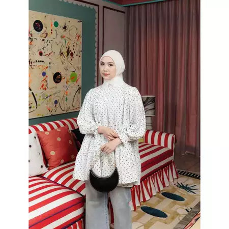 Woman standing in a room wearing white polka dot blouse by Haidee Orlin.