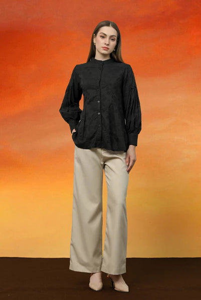 Person wearing a black Alia blouse by Kasa Heritage and beige pants against an orange and red gradient background