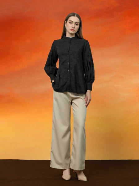 Person wearing a black Alia blouse by Kasa Heritage and beige pants against an orange and red gradient background