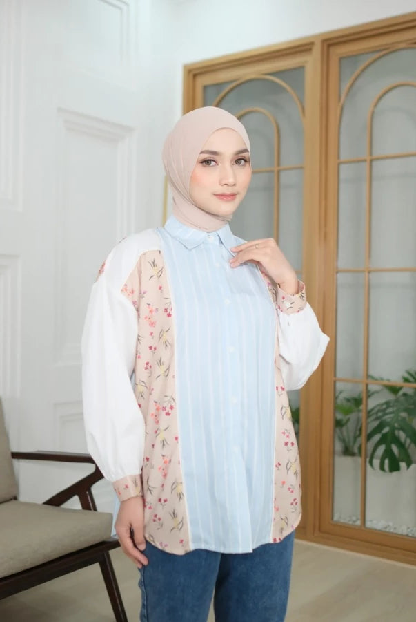 Woman wearing a light blue shirt by Abame with a floral details in a room with a wooden door and chair.