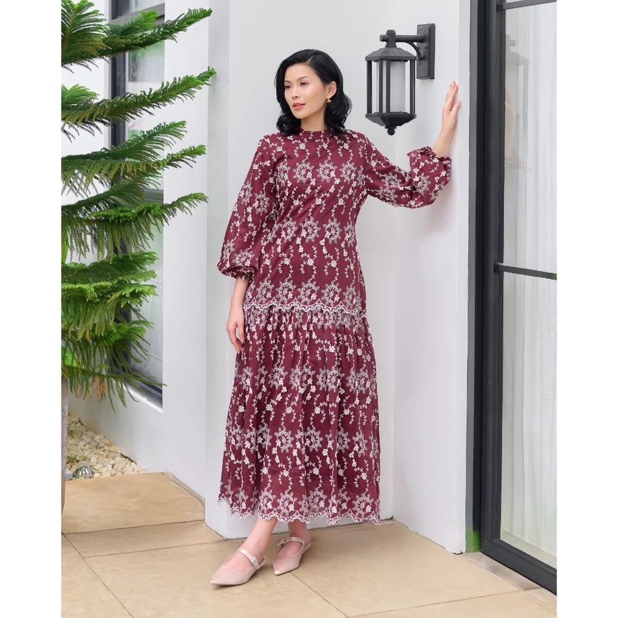 Woman in a maroon floral dress by Kasa Heritage standing in a modern interior setting with a plant and door.