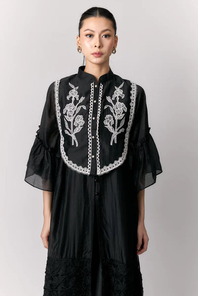 Woman wearing a black dress with white floral embroidery vest by Studio Tui on a plain background