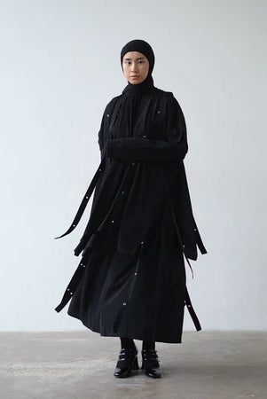 Person wearing a long black vest by Rashawl against a plain background