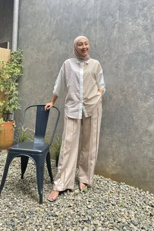 A person standing next to a metal chair wearing a beige shirt by Abame and matching pants with a round neckline, short sleeves, and a casual fit.