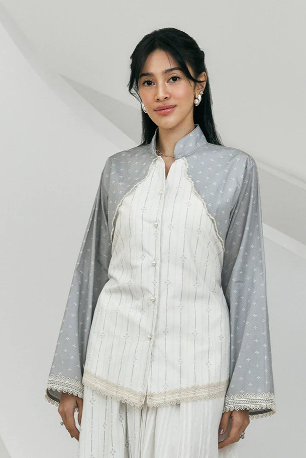 Woman wearing a white and gray women’s blouse by Studio Tui featuring a front button closure, mandarin collar, and delicate lace trim along the edges. Paired with matching bottoms for a refined and elegant look.