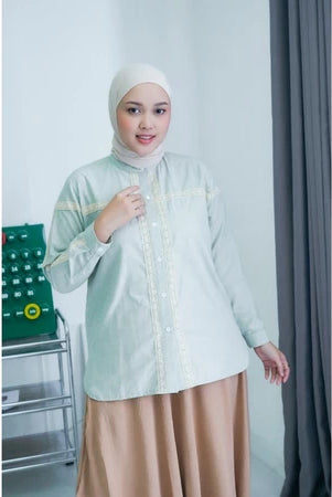 Woman wearing a light green shirt by Abame and beige skirt in an indoor setting