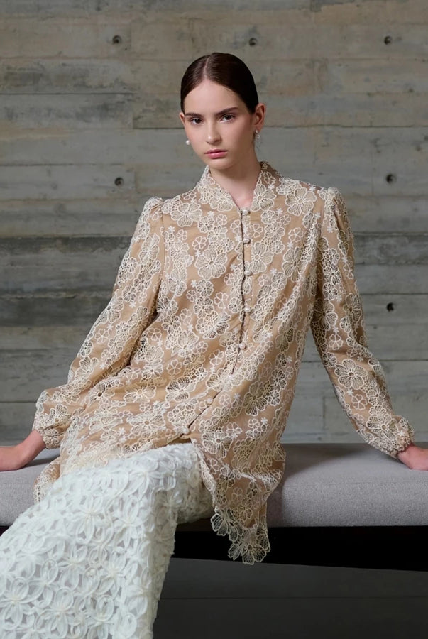 Woman wearing a beige lace long blouse by Kasa Heritage sitting on a bench against a wooden wall.