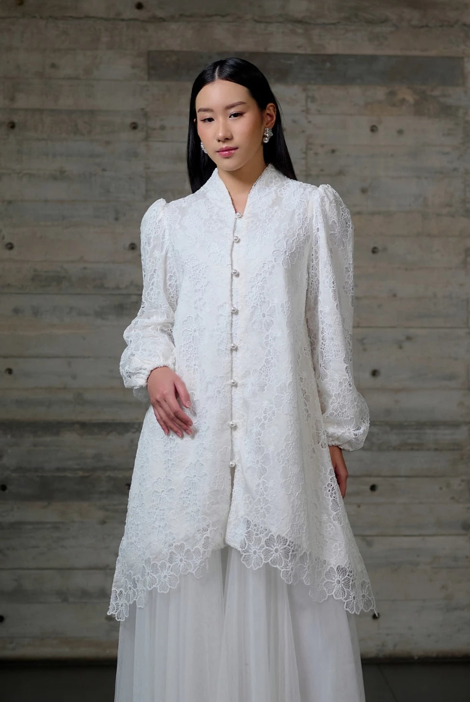 Woman wearing a white lace long blouse by Kasa Heritage against a wooden background.