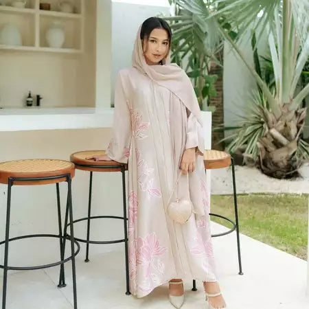 Woman in a floral abaya from Haidee Orlin standing in an outdoor setting with plants and furniture.