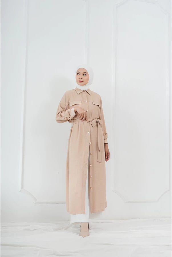 Woman wearing a beige long tunic by Abame against a white background.
Seorang wanita mengenakan tunik panjang berwarna beige dari Abame di latar belakang putih.
