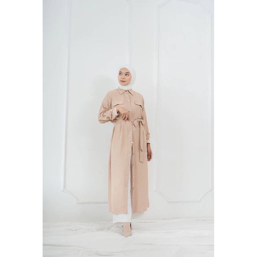 Woman wearing a beige long tunic by Abame against a white background.
Seorang wanita mengenakan tunik panjang berwarna beige dari Abame di latar belakang putih.