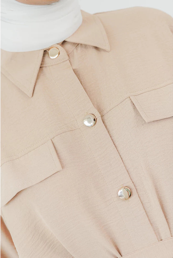 Close-up of a beige long tunic by Abame with button details on a white background.
Detail close-up dari tunik panjang berwarna beige dari Abame dengan detail kancing pada latar belakang putih.