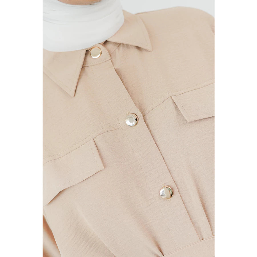 Close-up of a beige long tunic by Abame with button details on a white background.
Detail close-up dari tunik panjang berwarna beige dari Abame dengan detail kancing pada latar belakang putih.