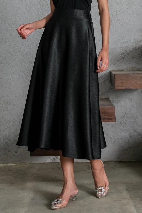 Person wearing a black satin skirt by Holy Peony in an urban setting with concrete walls and wooden steps.