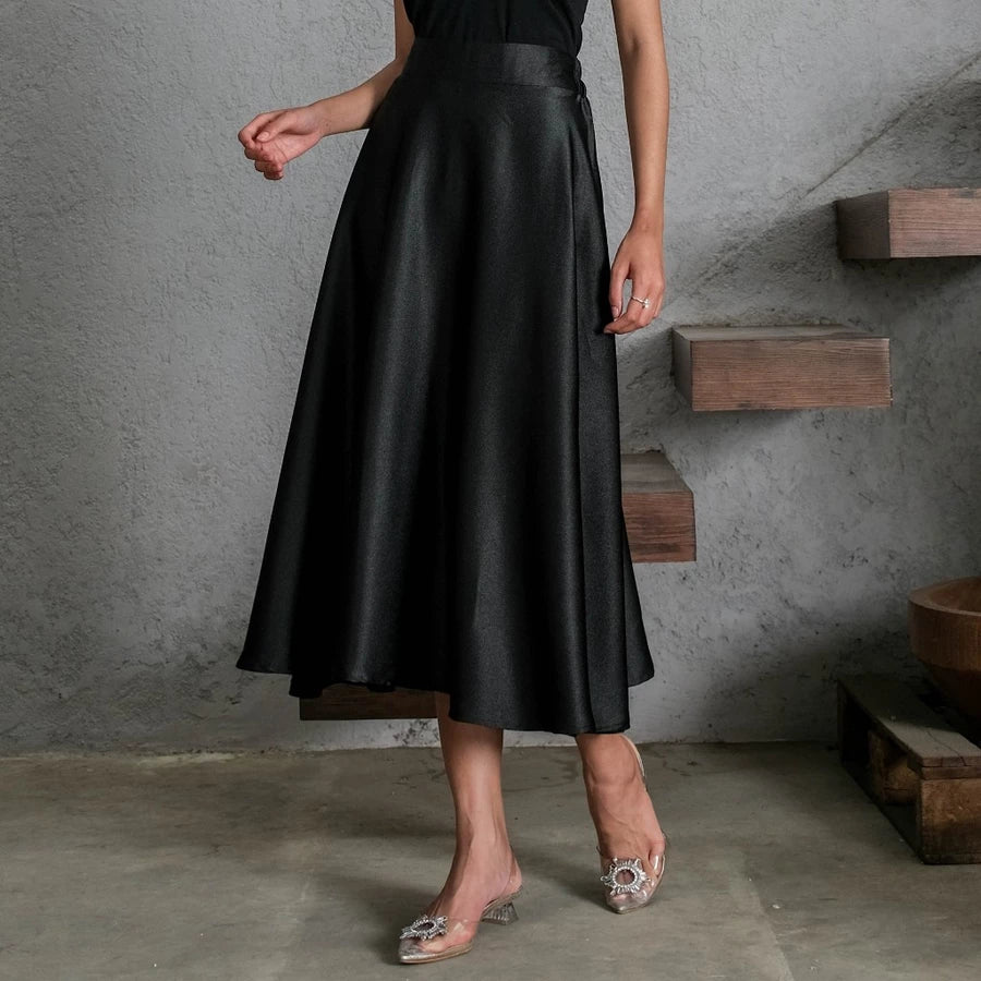 Person wearing a black satin skirt by Holy Peony in an urban setting with concrete walls and wooden steps.