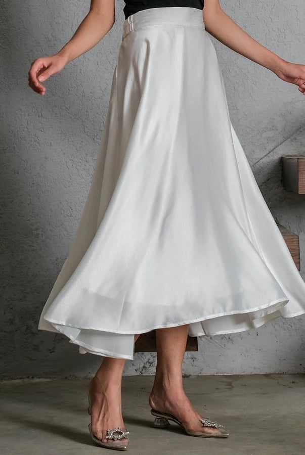 Person wearing a white satin skirt by Holy Peony with a gray concrete wall background