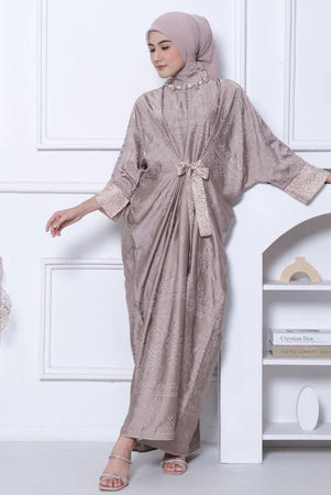 Woman in a light brown dress by Kartinis Label with a matching hijab standing in a minimalistic room.