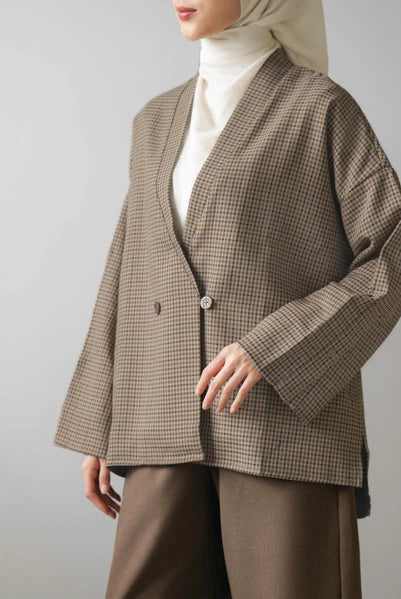 Person wearing a brown checkered blazer by Mistyvori over a white shirt with a beige hijab on a gray background