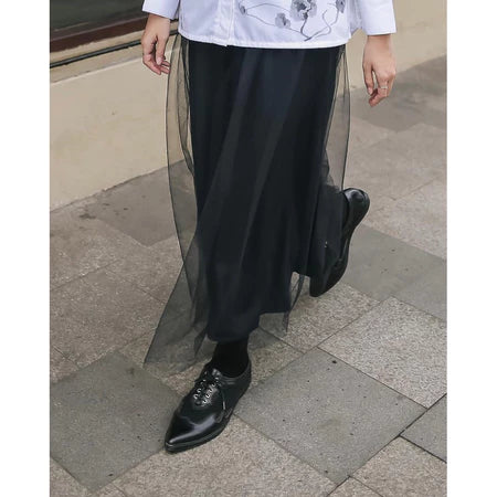 Person wearing a black skirt by Maima and black shoes on a pavement.