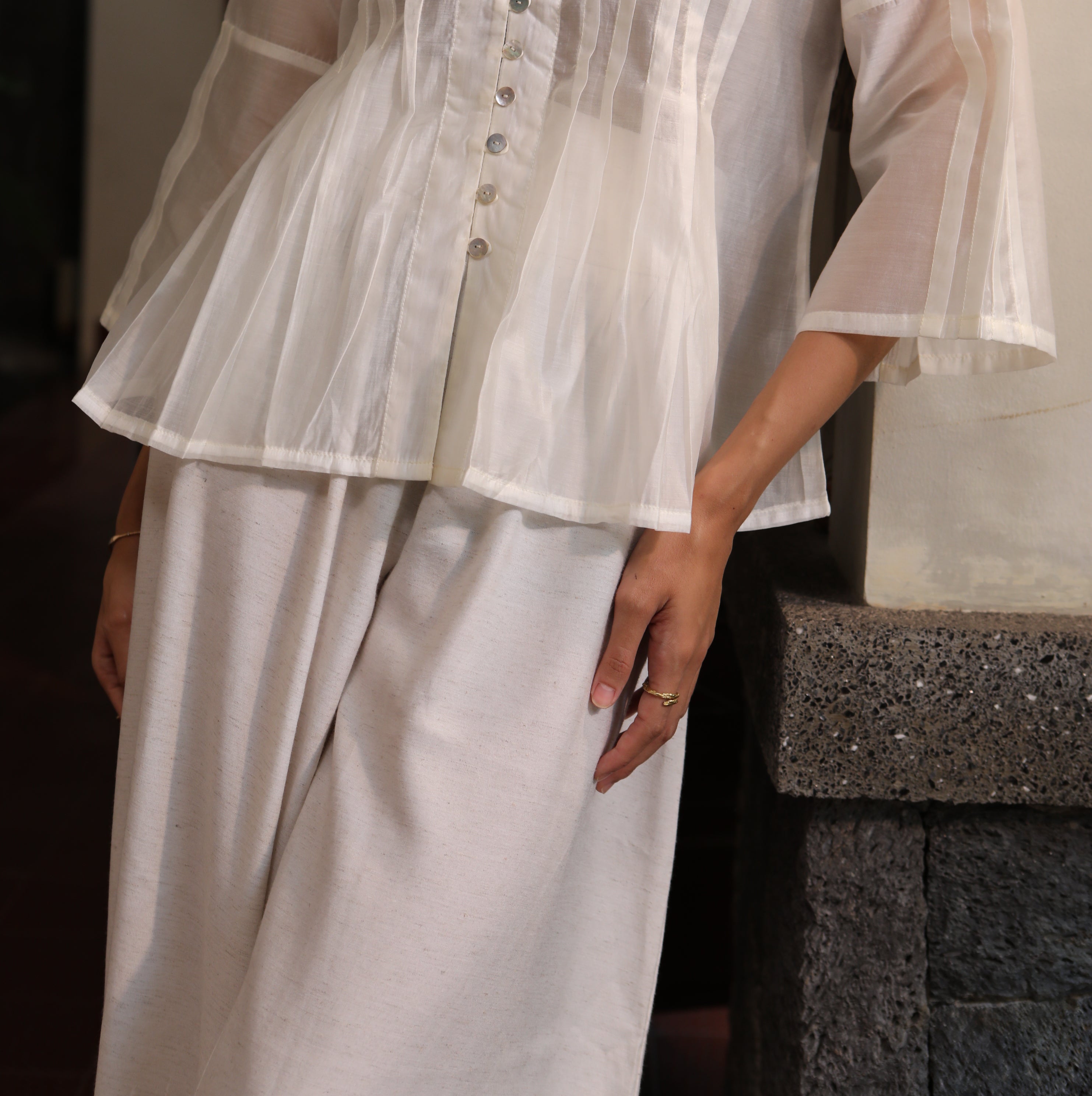White blouse by Kasyalia with sheer overlay held by a person on a neutral background