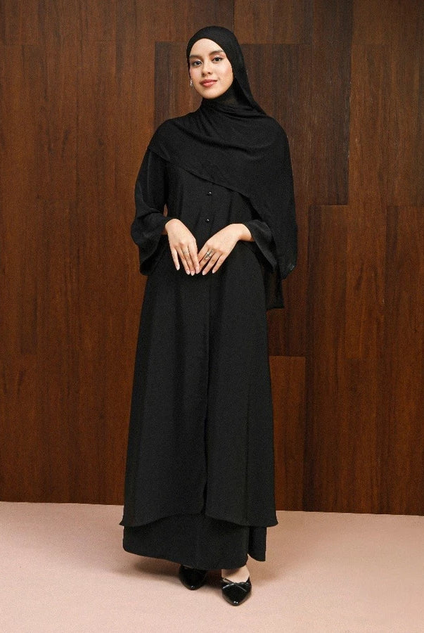 Woman wearing a black abaya dress by Lozy Hijab against a wooden background