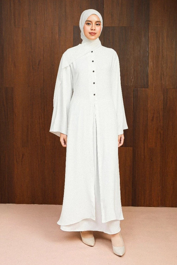 Woman wearing a broken white abaya dress by Lozy Hijab with a hijab against a wooden background