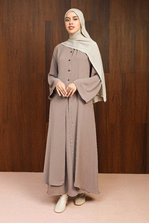 Woman wearing a long, light brown abaya dress by Lozy Hijab with a hijab against a wooden background