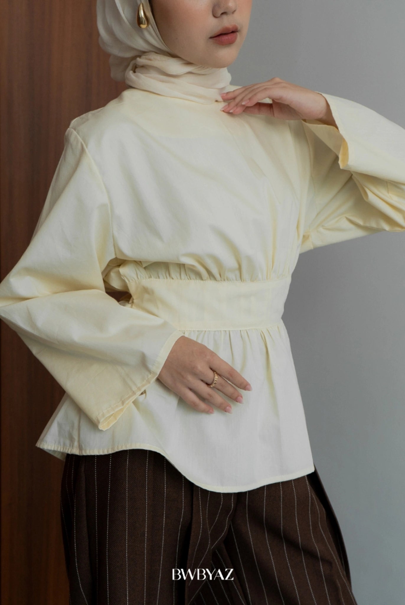 Person wearing a cream-colored blouse with wide sleeves by BWBYAZ against a neutral background