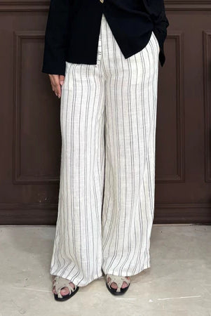 Person wearing white pants with black stripe by Renaette with a black top against a brown paneled wall.