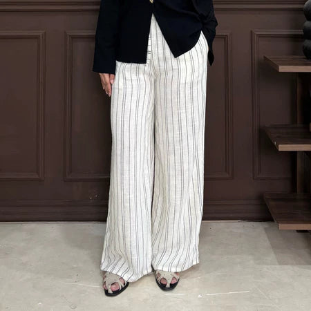 Person wearing white pants with black stripe by Renaette with a black top against a brown paneled wall.