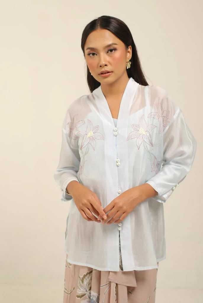 Woman wearing a light blue kebaya by Kartinis Label with floral patterns on a beige background