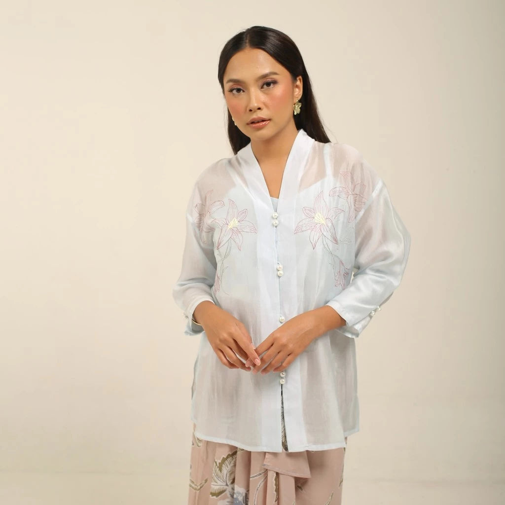 Woman wearing a light blue kebaya by Kartinis Label with floral patterns on a beige background