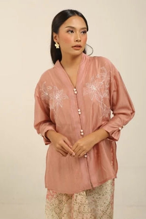 Woman wearing a pink embroidered kebaya by Kartinis Label with a plain background