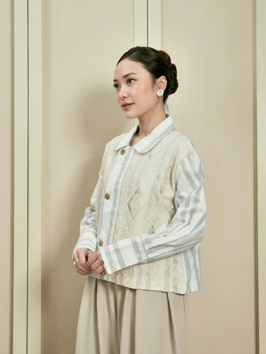 Woman wearing a light-colored stripped outer by Studio Tui with a patterned against a beige background