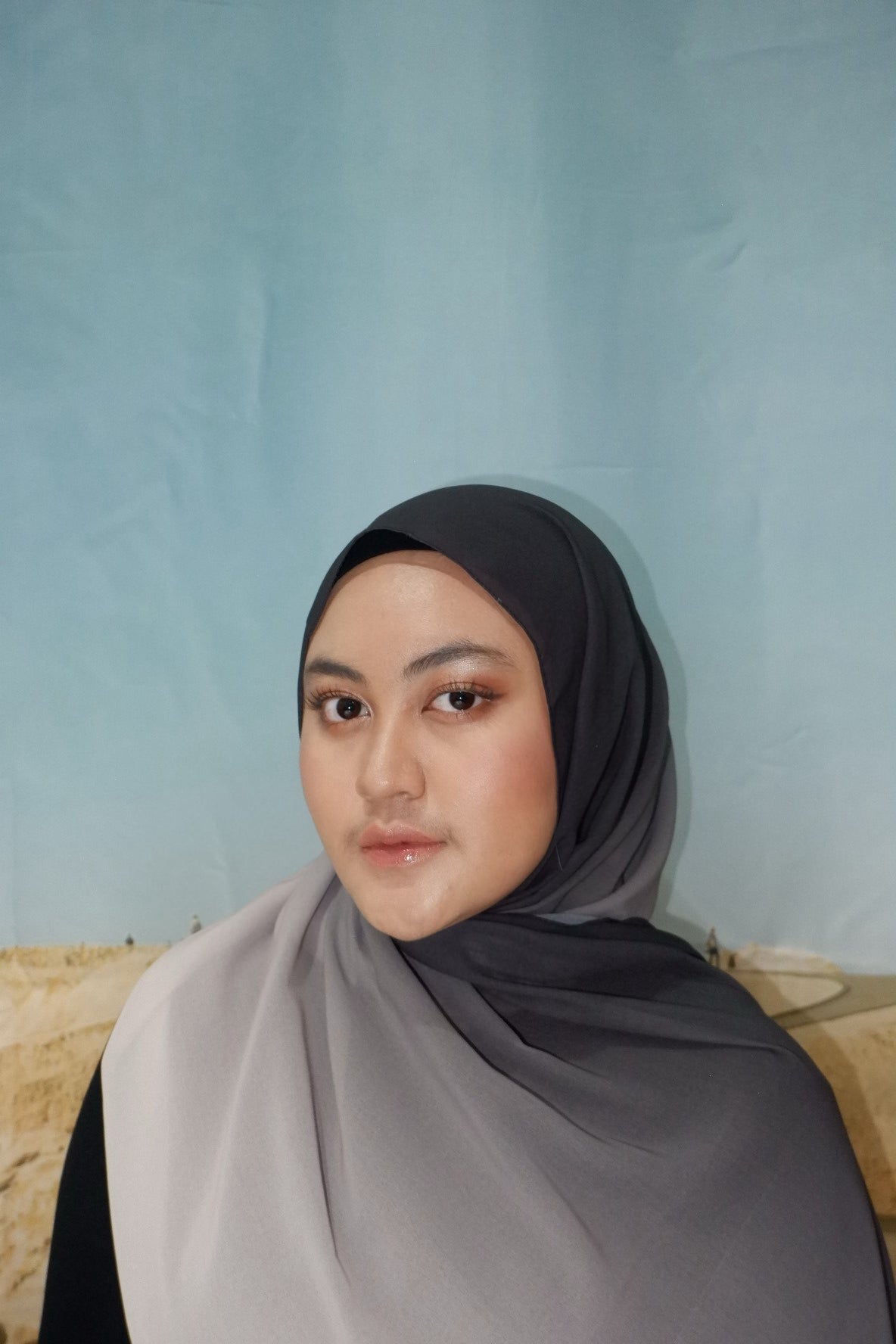 Woman wearing a gray pashmina hijab against a light blue background