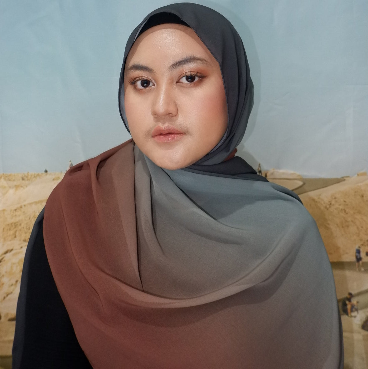 Woman wearing a pashmina hijab against a plain background