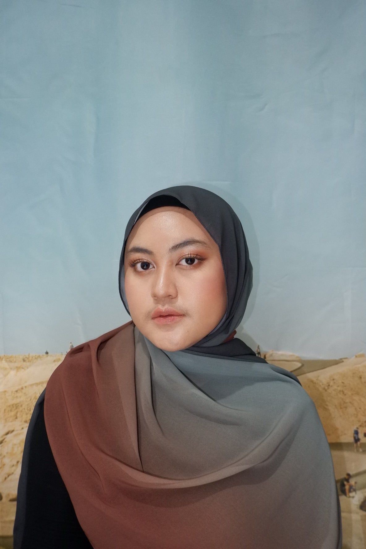 Woman wearing a pashmina hijab against a plain background