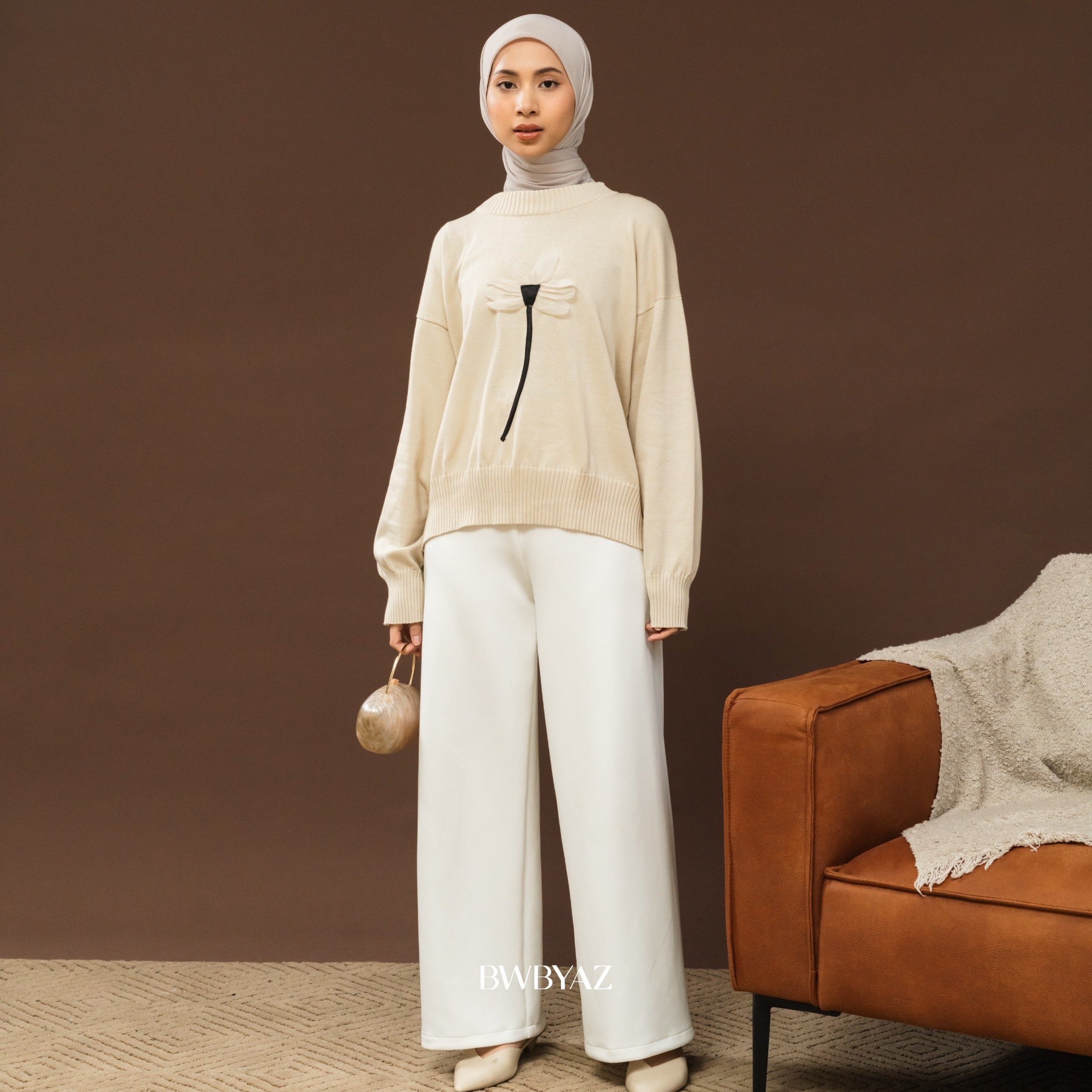 Person wearing a broken white sweater with a floral design from BWBYAZ, holding a beige handbag against a neutral background.