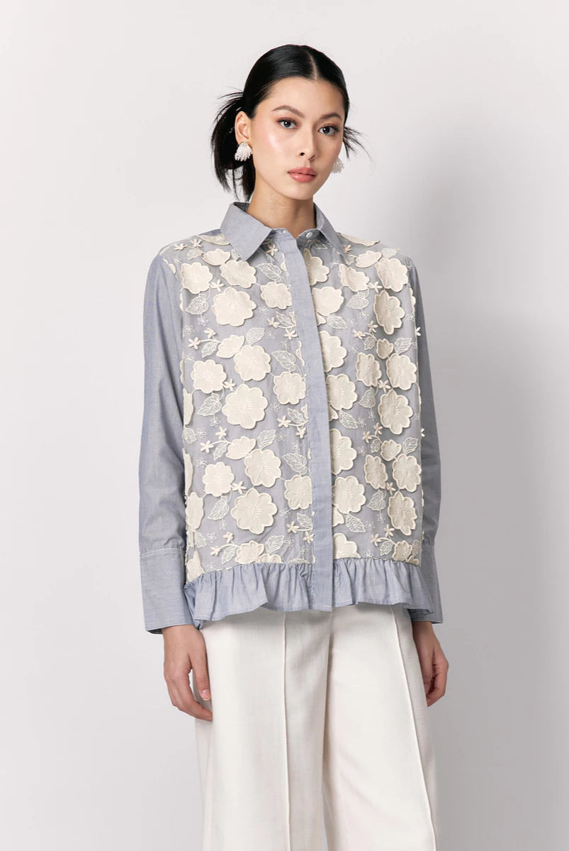 Woman wearing a light blue shirt by Studio Tui with floral lace overlay on a plain background