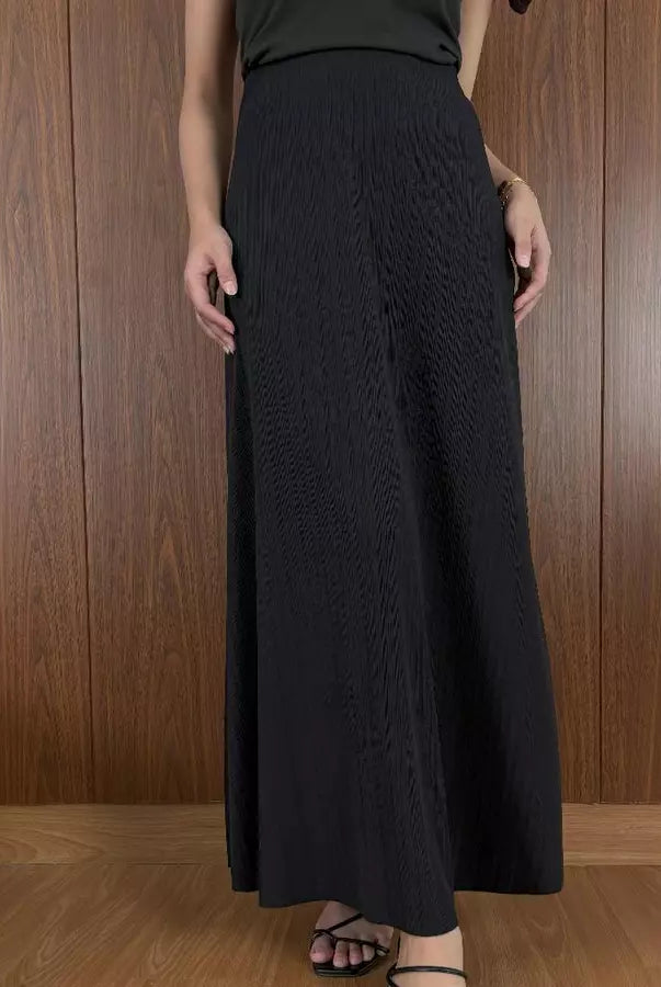 Person wearing black textured skirt by Renaette against a wooden panel background